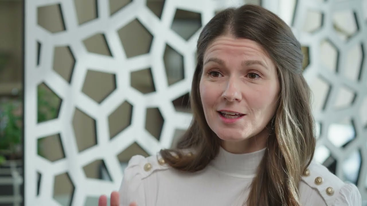 Woman speaking in front of patterned backdrop.