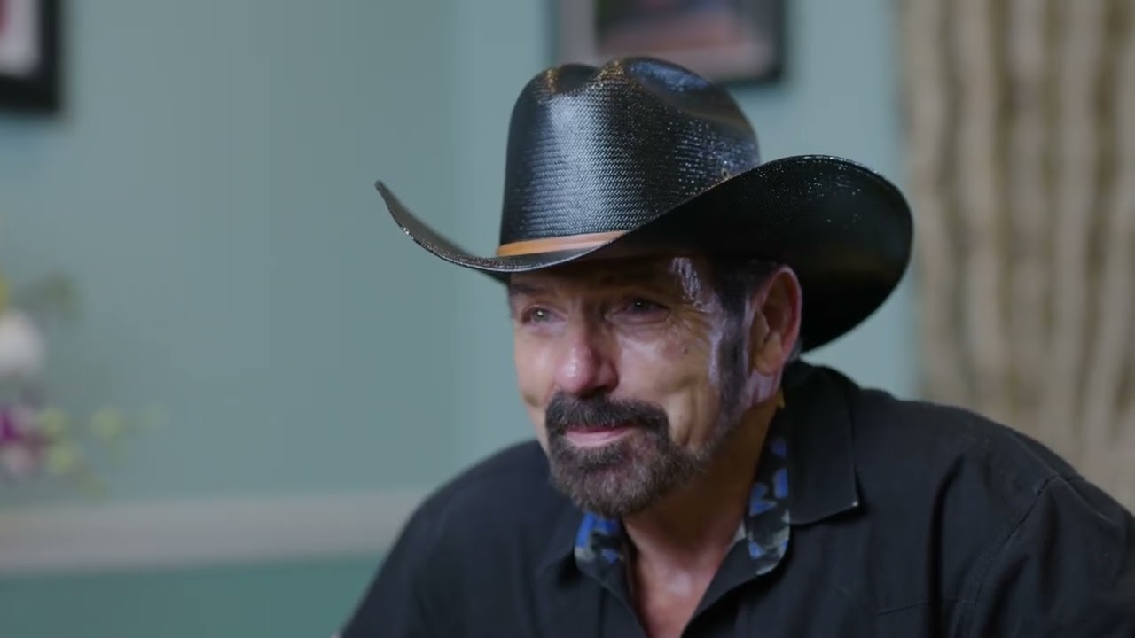 Man in cowboy hat smiling warmly indoors.