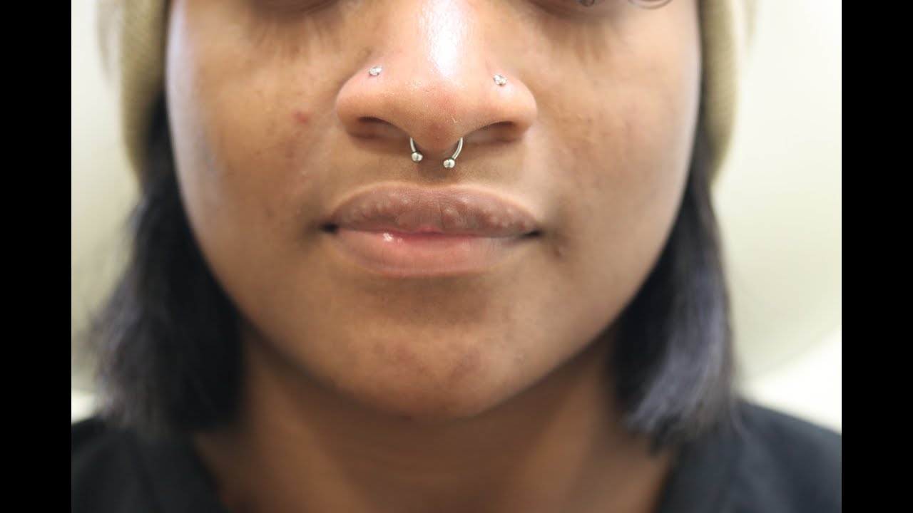 Person with multiple facial piercings and short hair.