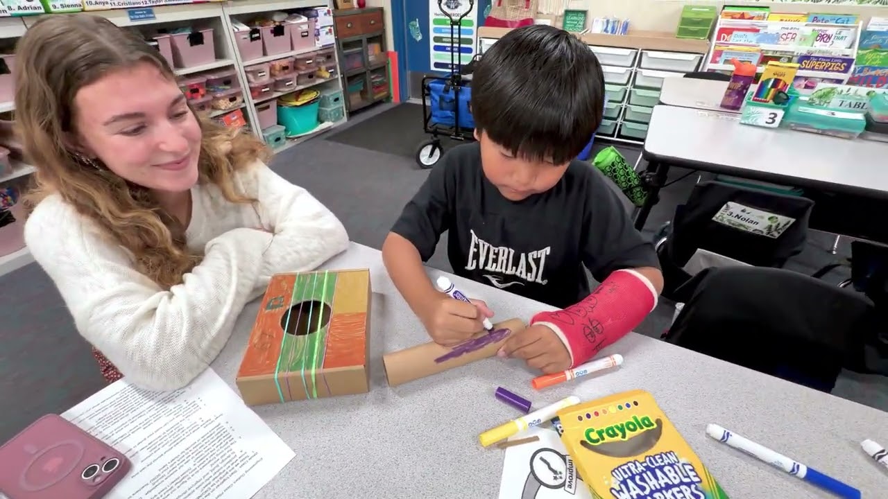 Teacher candidate nd Heritage Elementary student working on building a guitar out of cardboard boxes and tubes