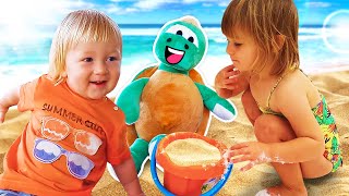 Bianca and Carl are playing with sand toys at the beach and cook toy food for a toy turtle.