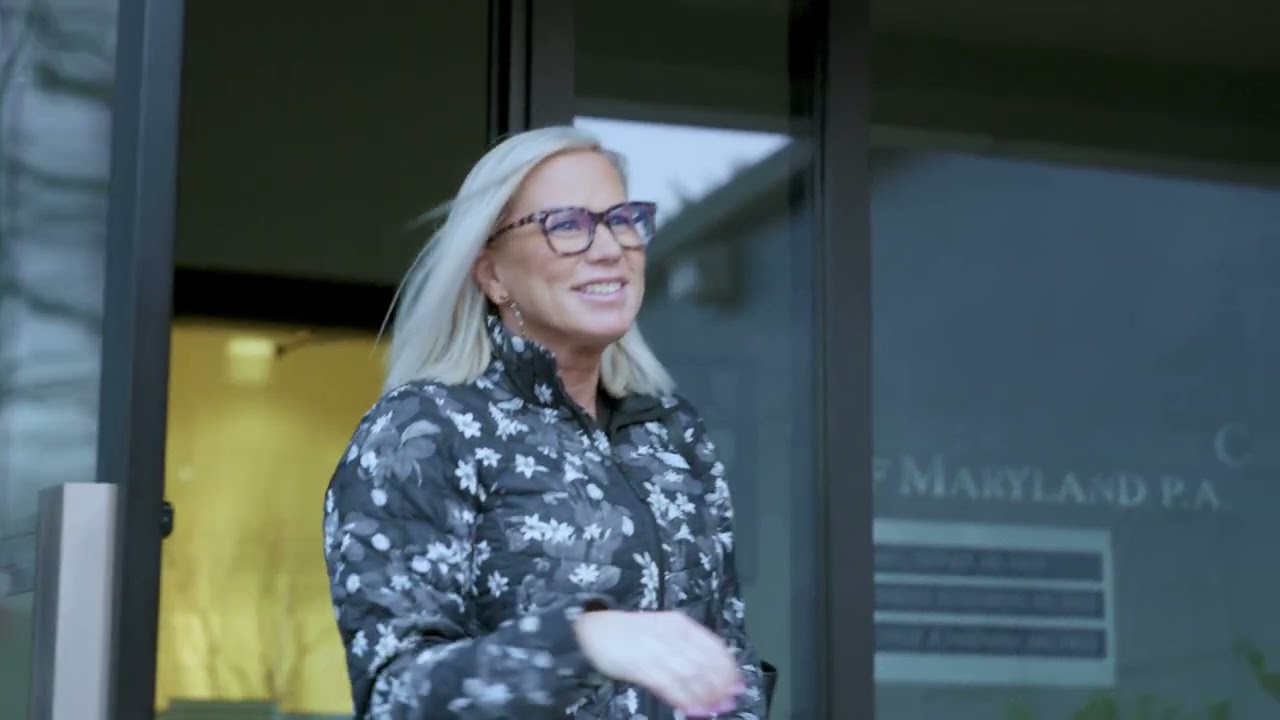 Smiling woman exiting a building, wearing glasses.