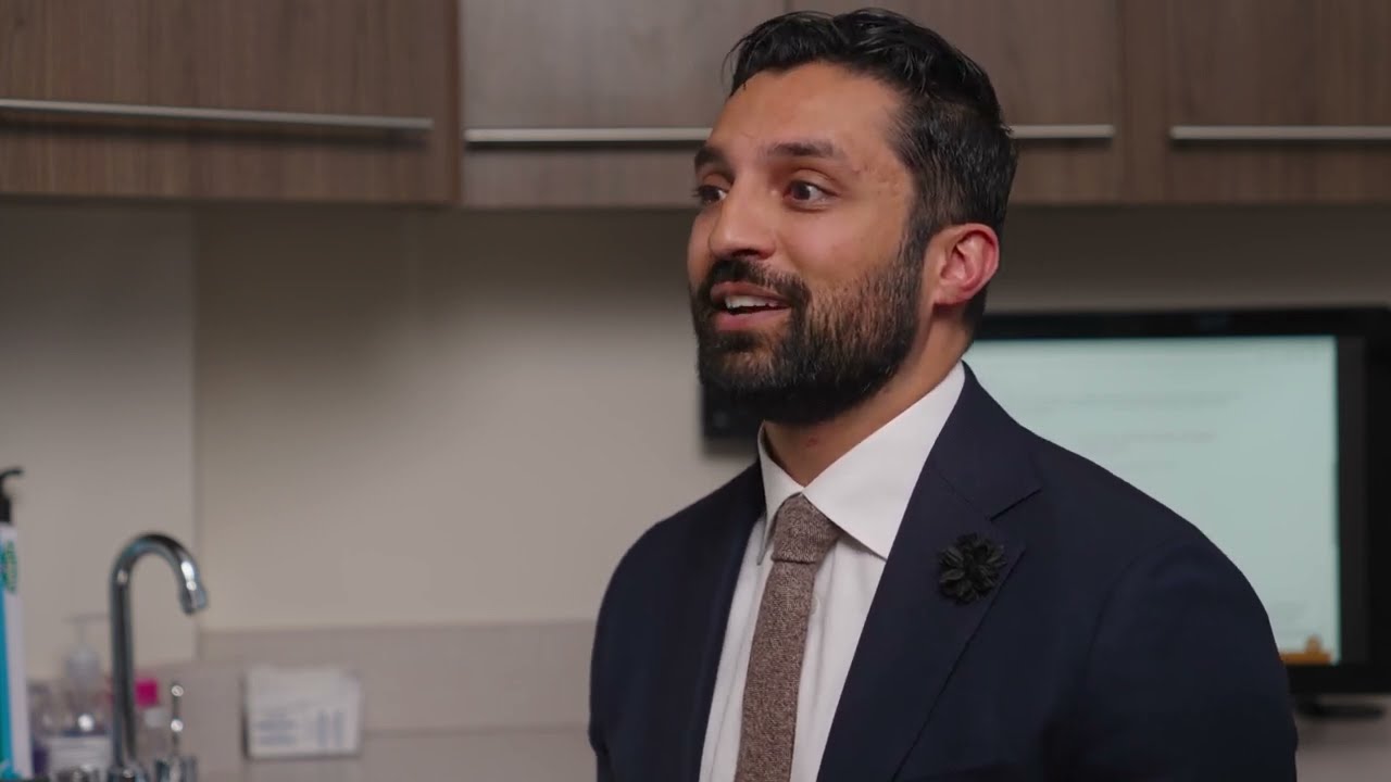 Man in a suit speaking in modern kitchen setting.
