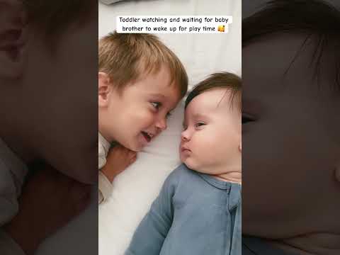 Adorable siblings laying in bed with the toddler watching & waiting for his baby brother to wake up