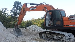 The excavator Doosan DX 225 CA is leveling the rock field and moving it to the dump truck