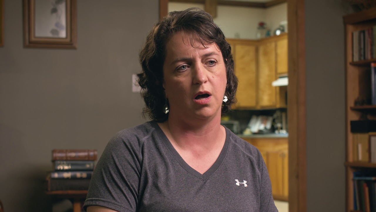 Woman sitting indoors, looking contemplative.