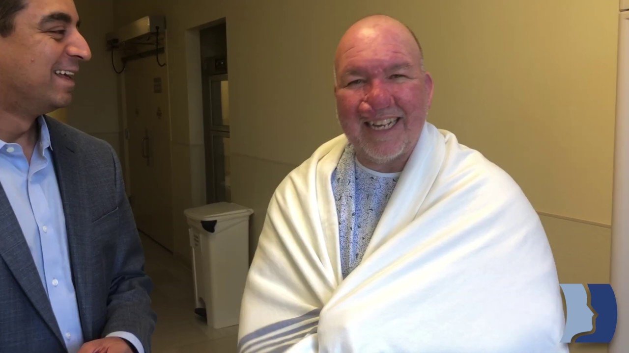 Smiling man wearing a blanket in a hallway.