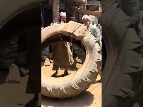 An elderly man is working on repairing a large puncture in the tire of a large tractor.