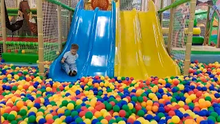 A child is playing on a playground and sliding down a slide with colorful balls.